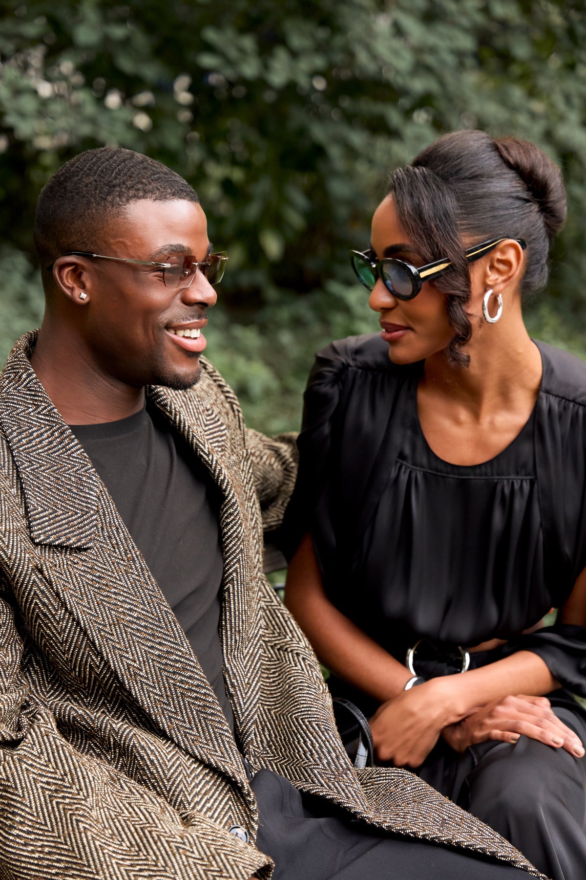 Couple in sunglasses seated outdoors in front of greenery