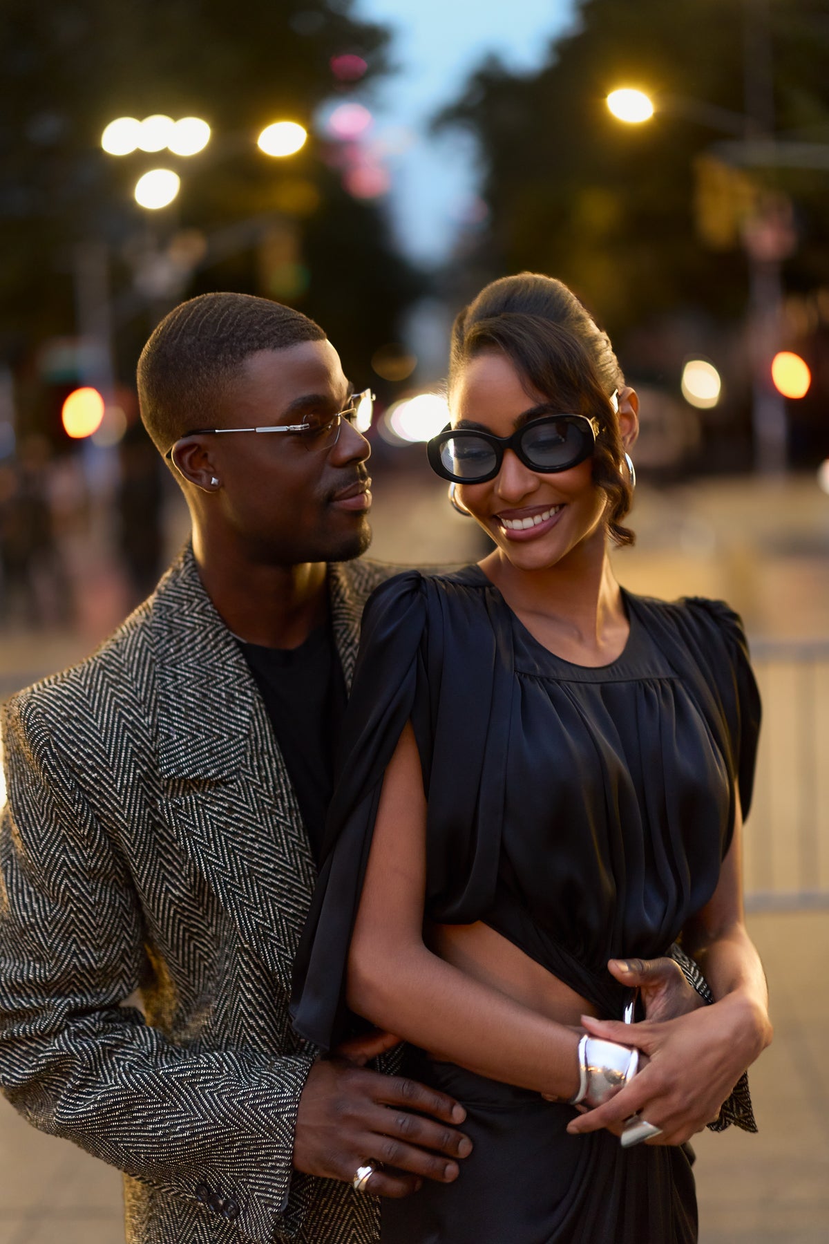 Couple in sunglasses embracing on a city street at dusk